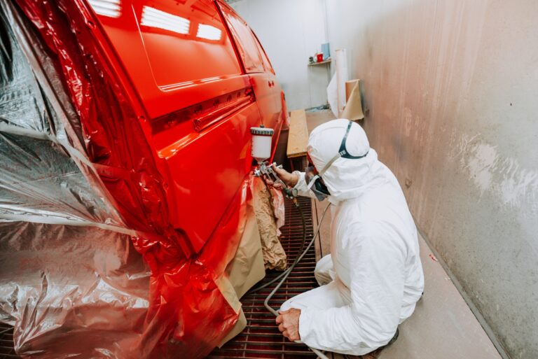 Portrait of Painter working and painting a red car in paint garage