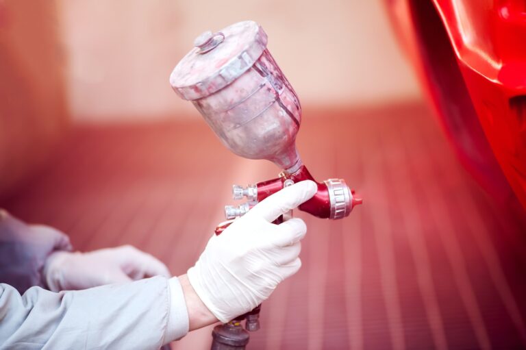 Worker painting a red car in paiting booth using professional tools